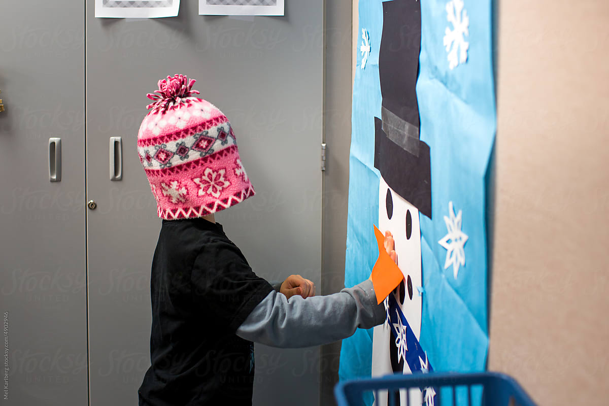 Boy in school classroom sticking nose on a paper snowman