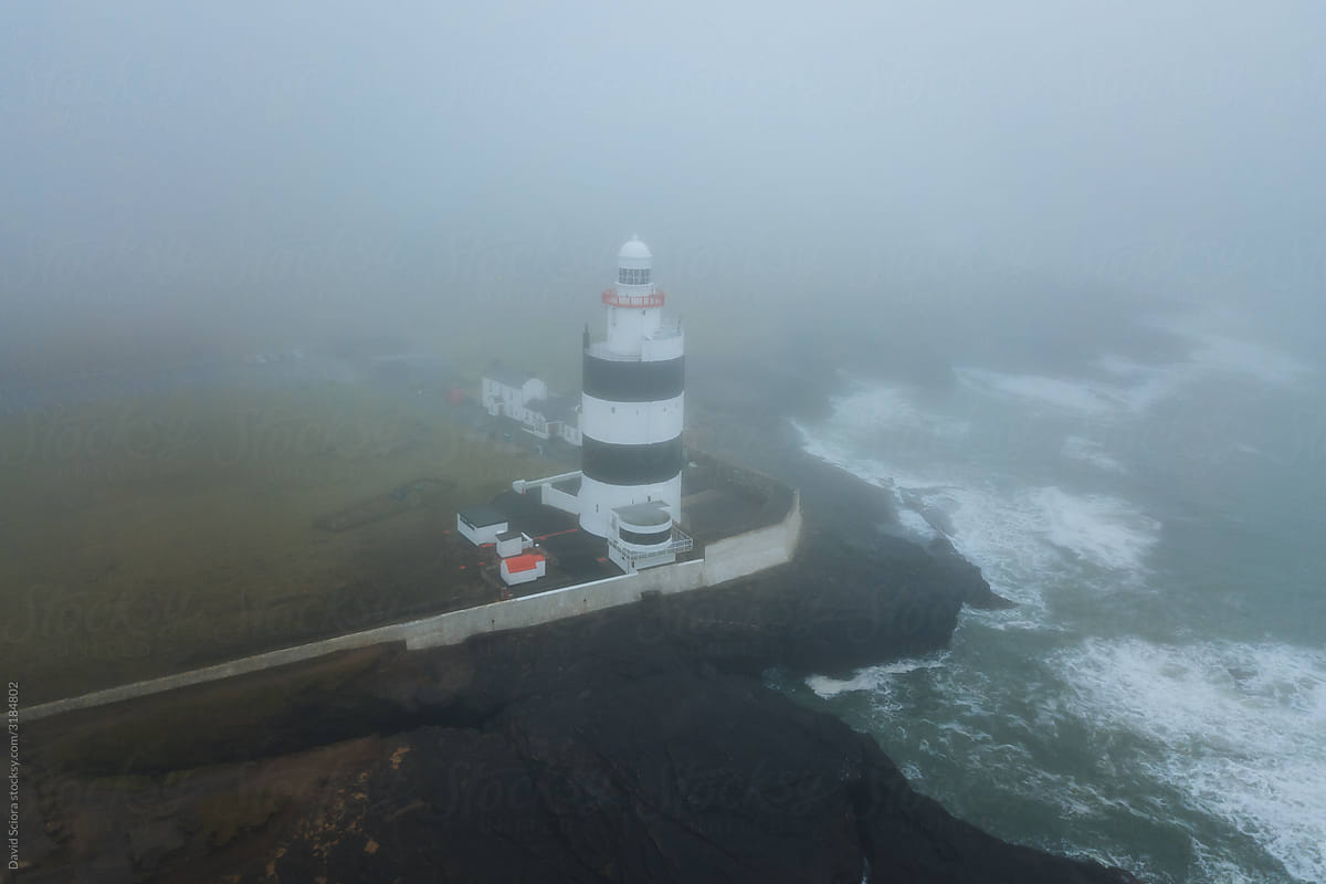 Aerial view of the lighthouse in the fog with rocks and rough sea.
