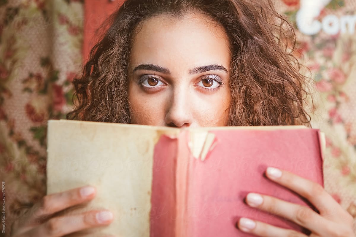 Beautiful Young Woman Holding an Old Book in front of her Face
