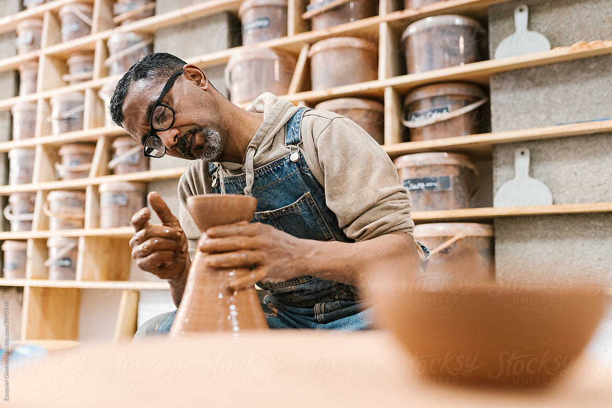 Black craftsman examining clay vase on wheel