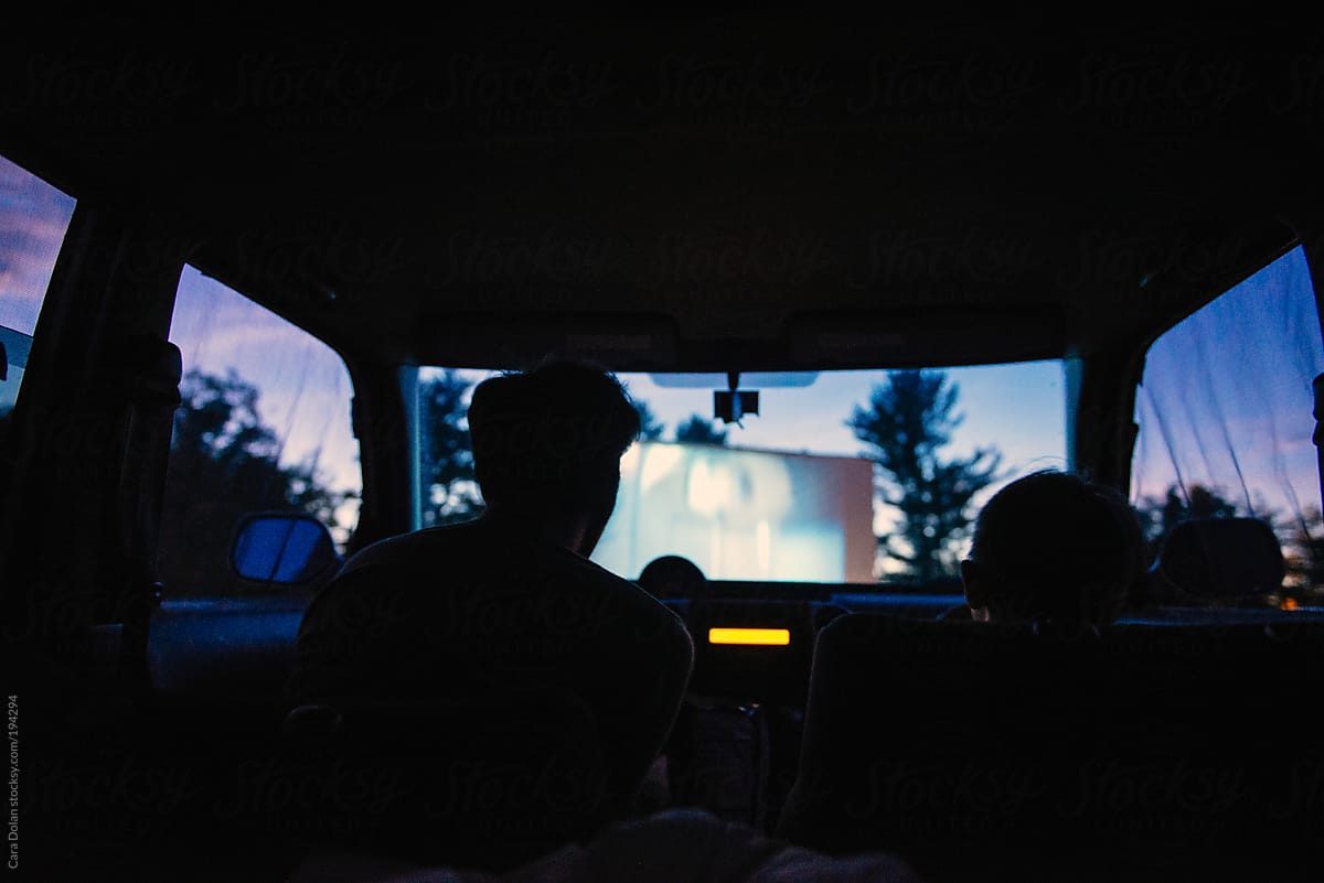 Boy and his dad watch a drive-in movie together in the car on a summer night