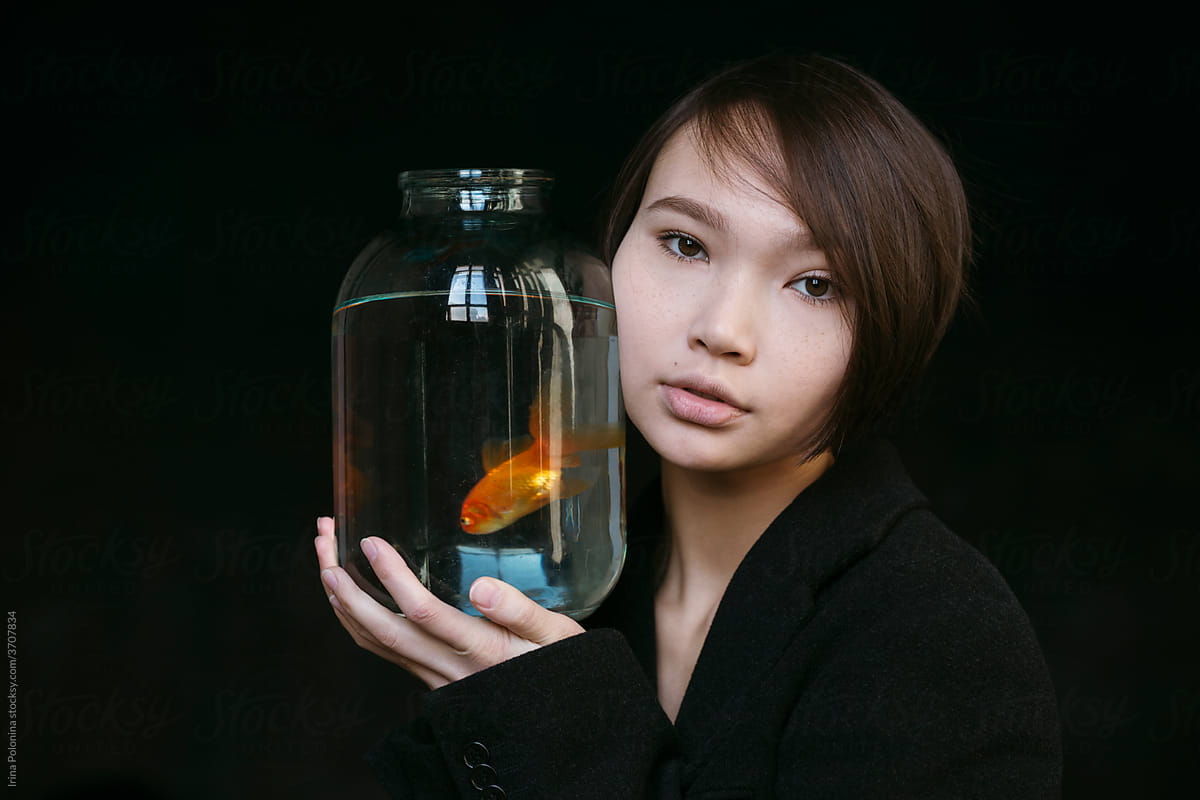 Asian girl with an aquarium fish in a dark room.