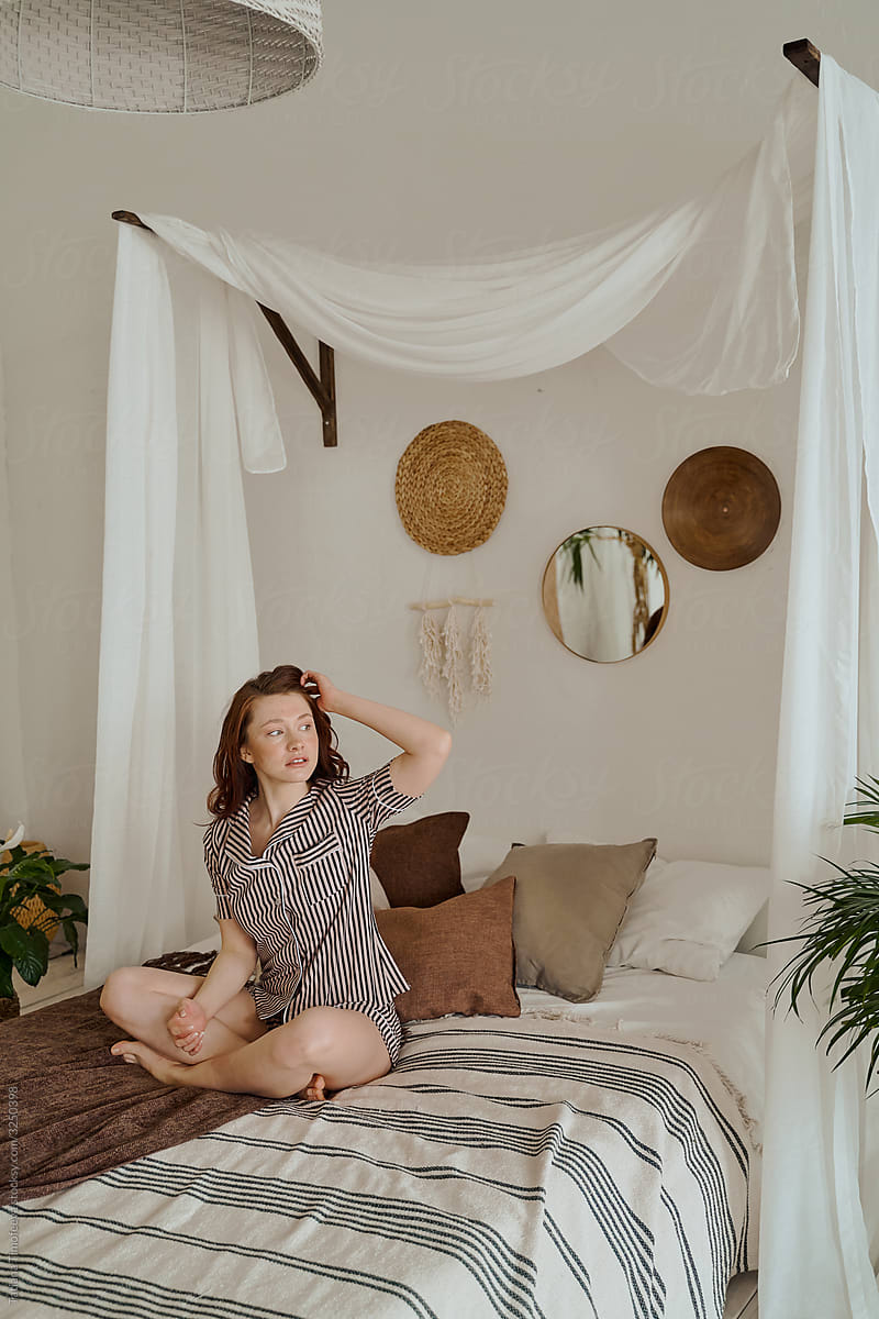 a beautiful girl in striped pajamas is sitting on a bed with a white canopy