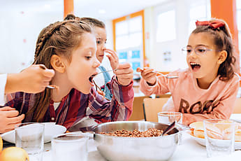 Two Funny Kids Looking At Camera While Eating In School Canteen by Stocksy  Contributor VICTOR TORRES - Stocksy