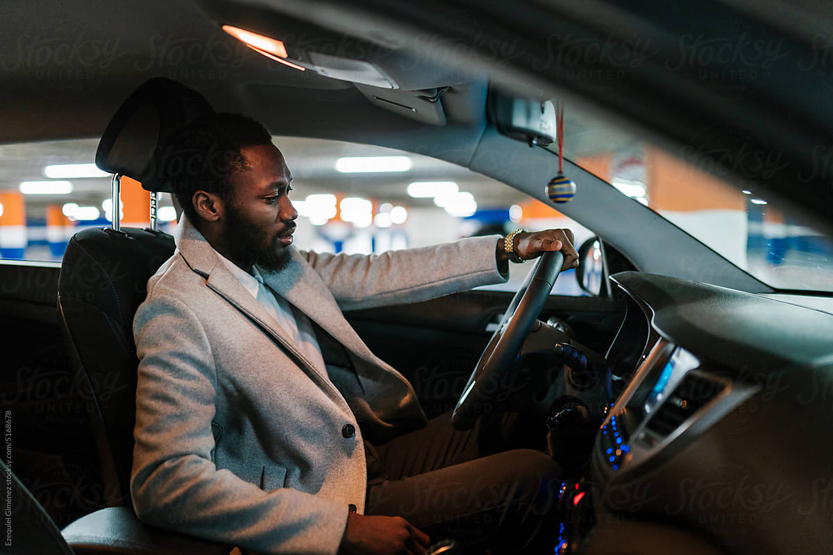 Black businessman sitting behind car wheel