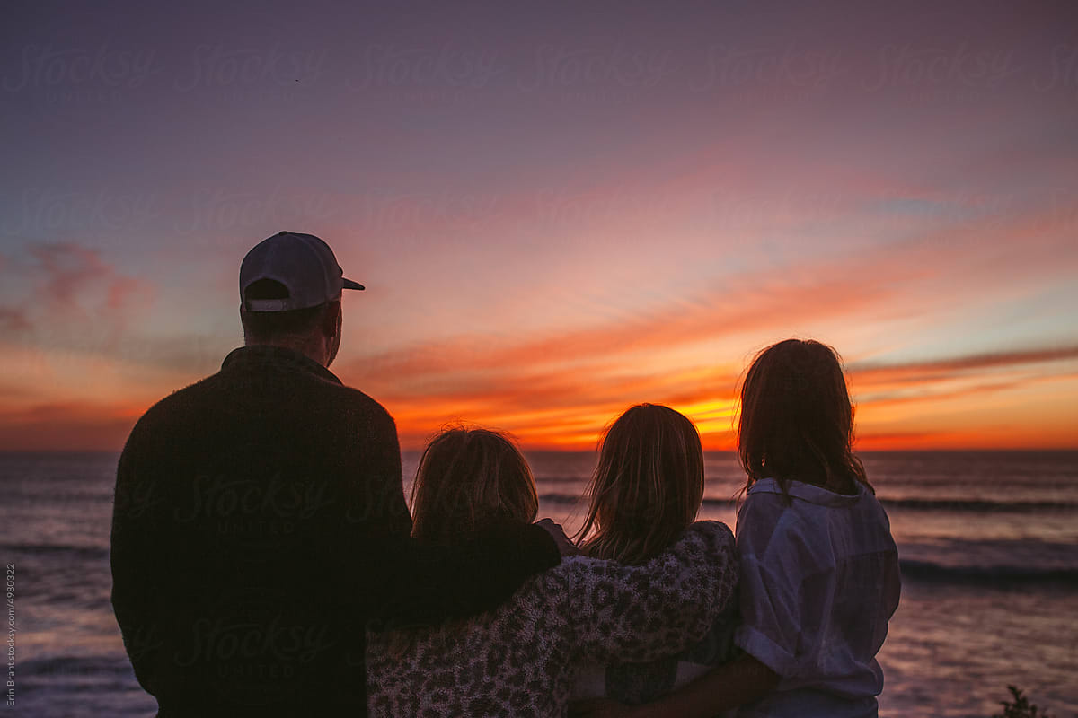 Family of with teenagers standing at the beach watching the sunset