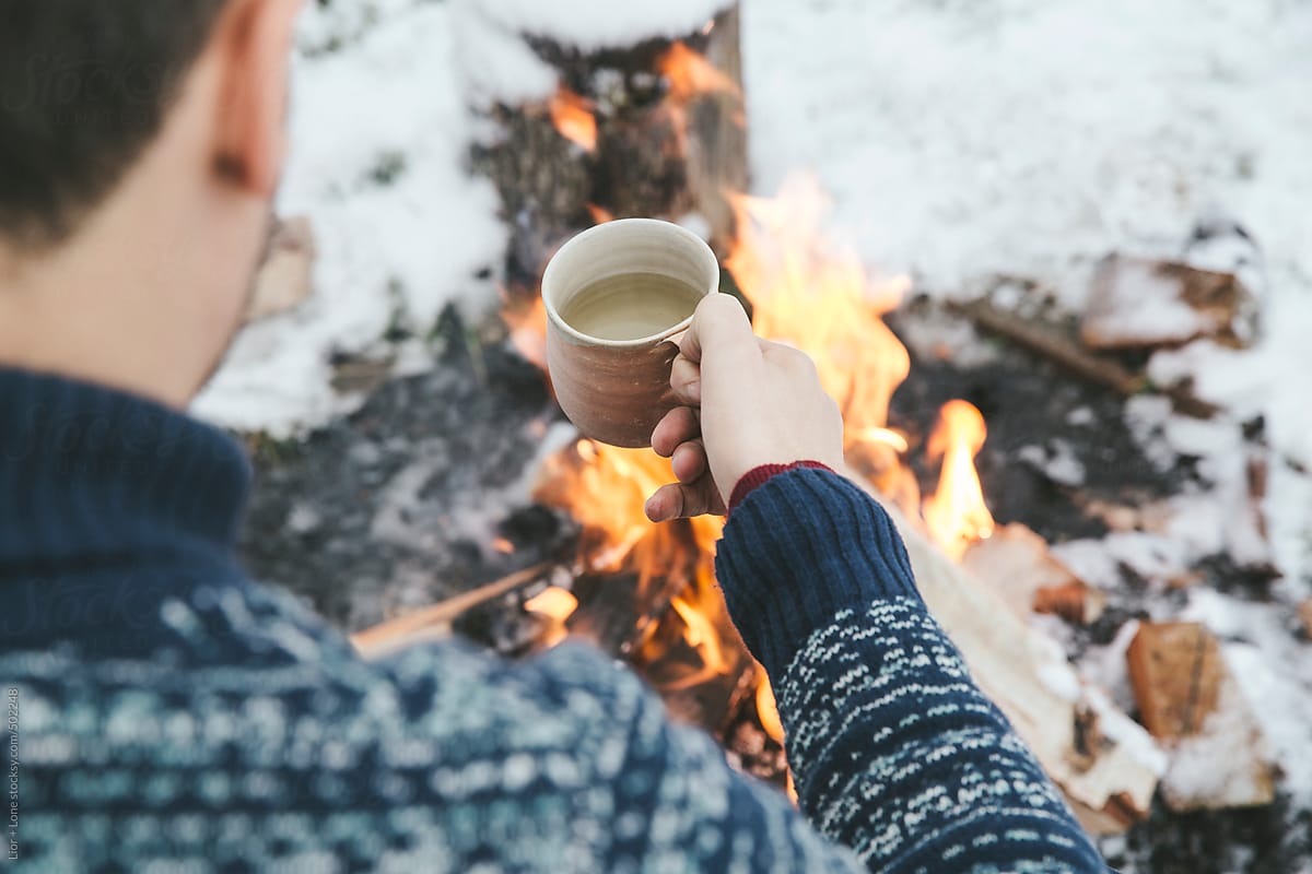 Man having hot tea next to bonfire in the snow