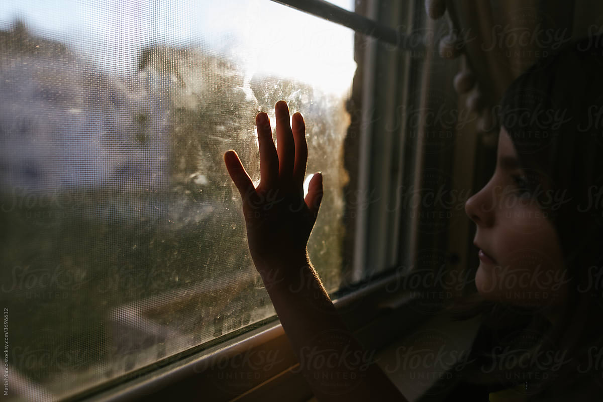 Child\'s hand touching window as she gazes out window