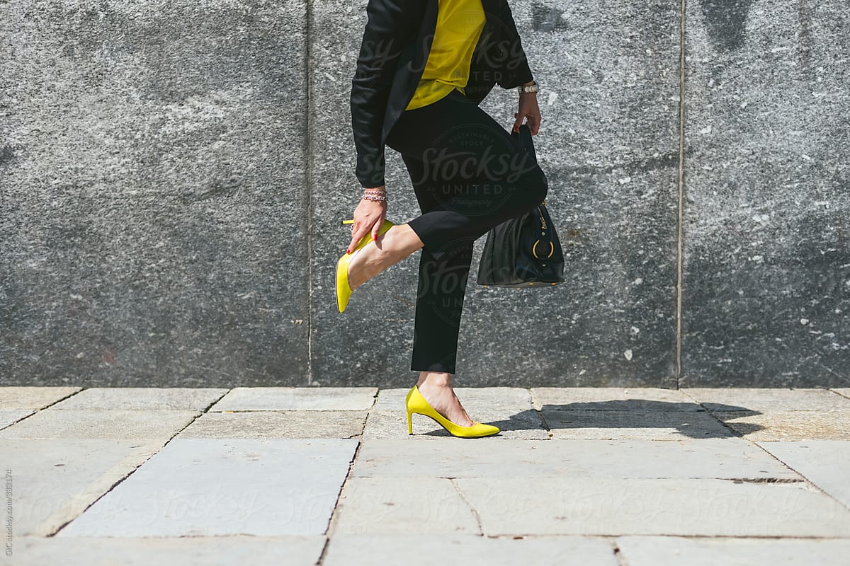 Woman touching her yellow heel in the street