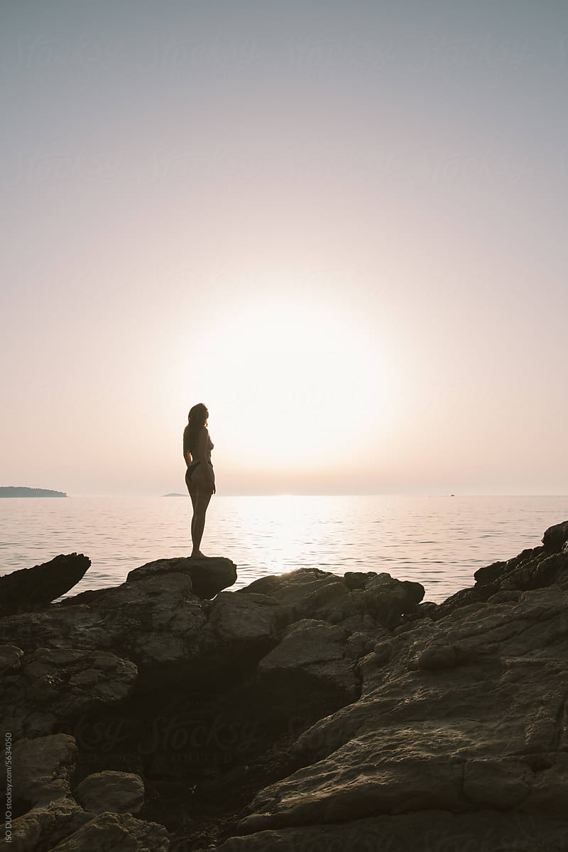 Woman standing on the rock and watching sunset