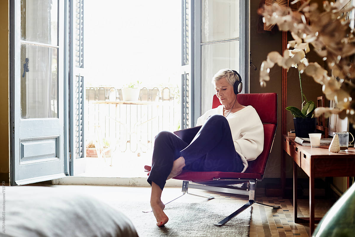 Senior Woman Listening Music While Sitting On Chair At Home