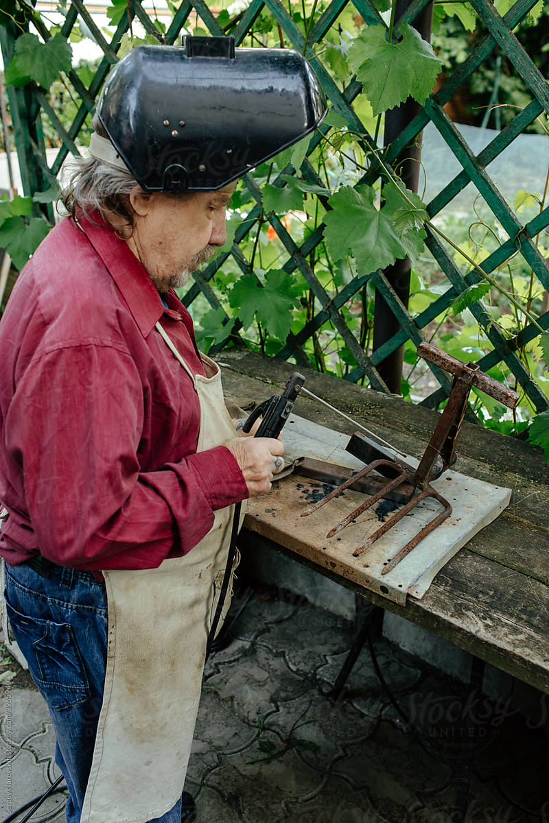 Senior man with welding tool working in garden