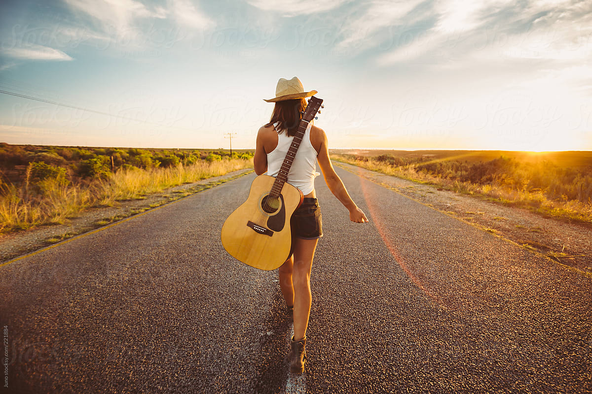 Female musician with a guitar hitchhiking on an open country road