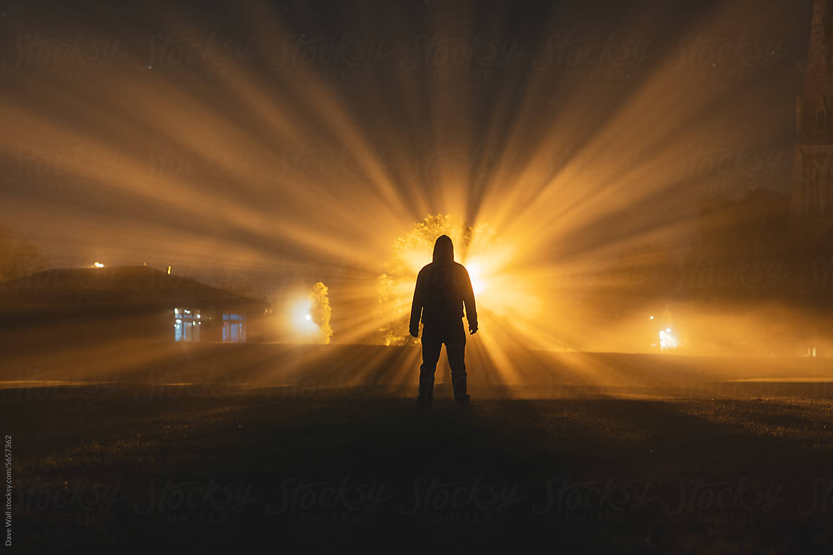 A figure silhouetted against a street light at night