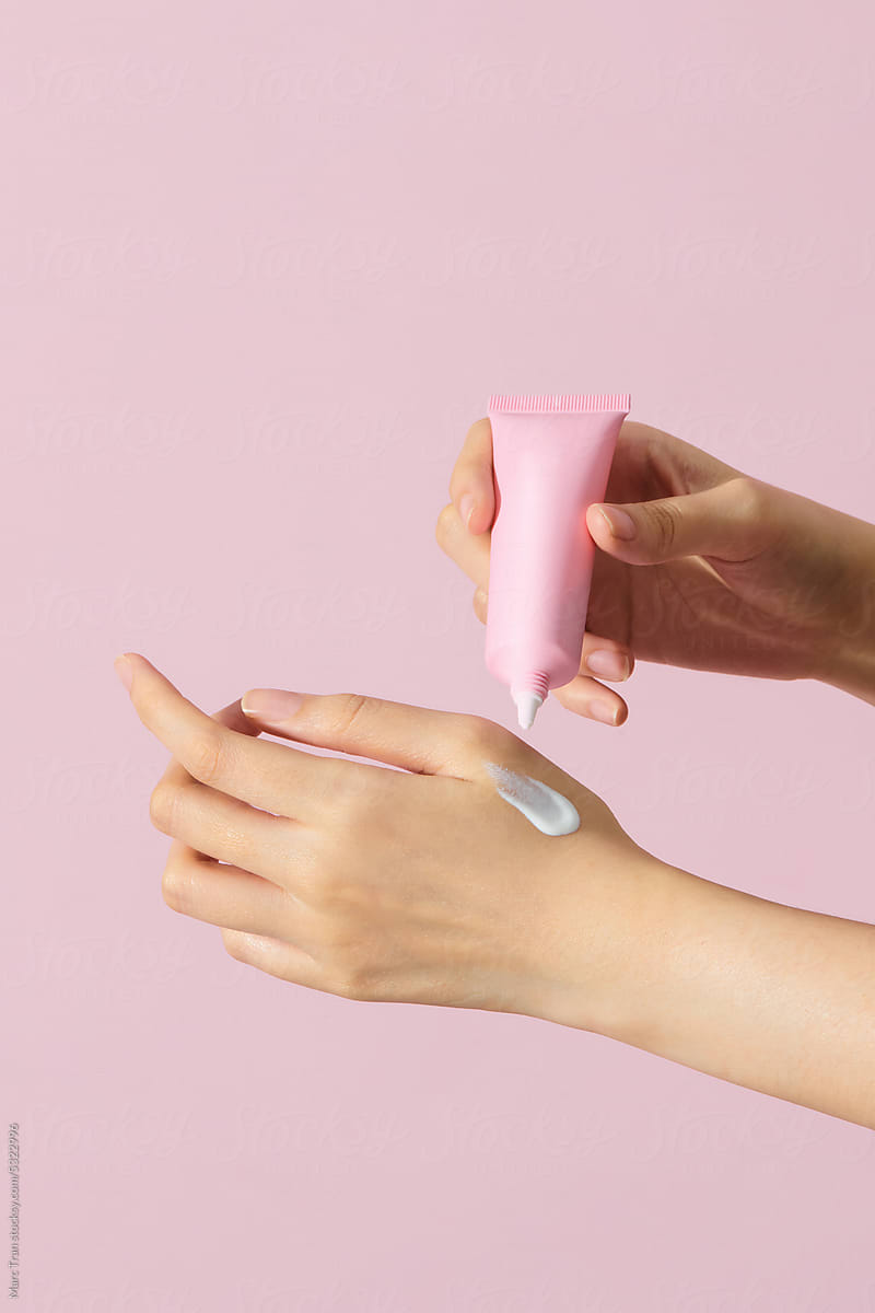 Women applying cream to her hands isolated on a pink background.