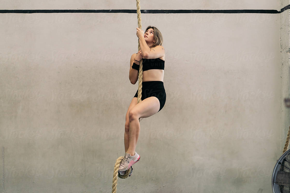 Woman climbing the rope in the gym.