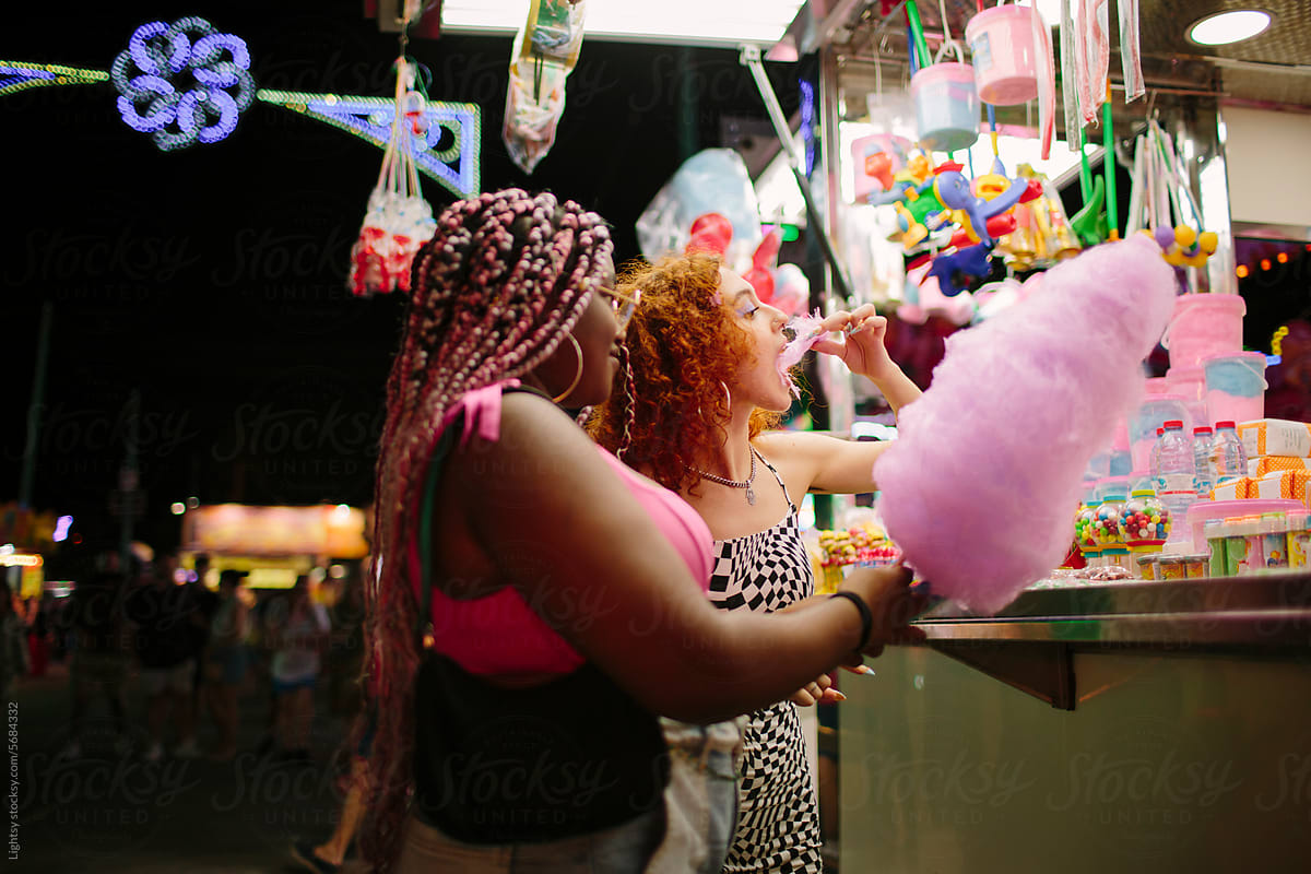 Young people having cotton candy at a fair at night