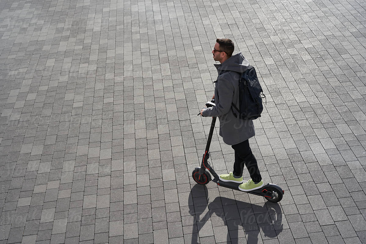 Man riding electric scooter on paving on sunny day