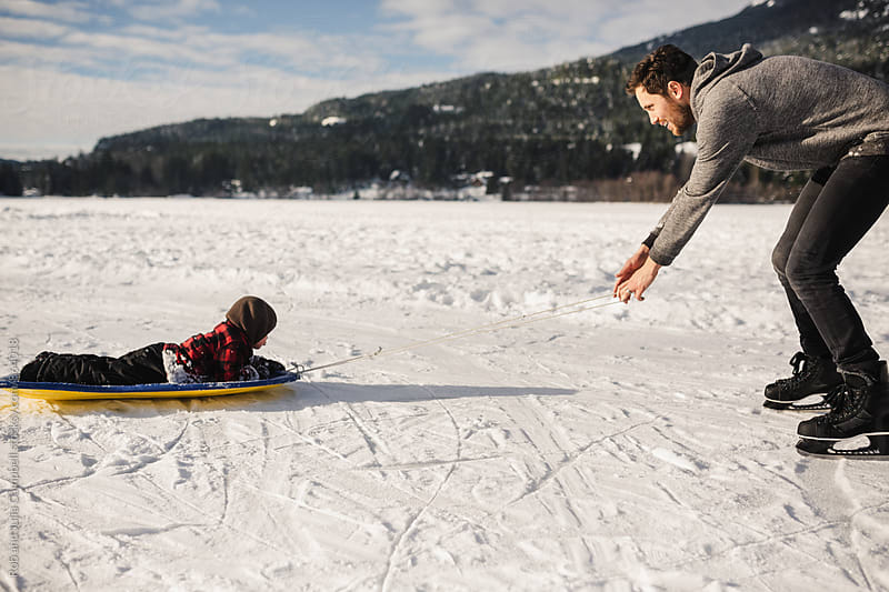 Active young dad pulling son on sled on frozen lake in winter