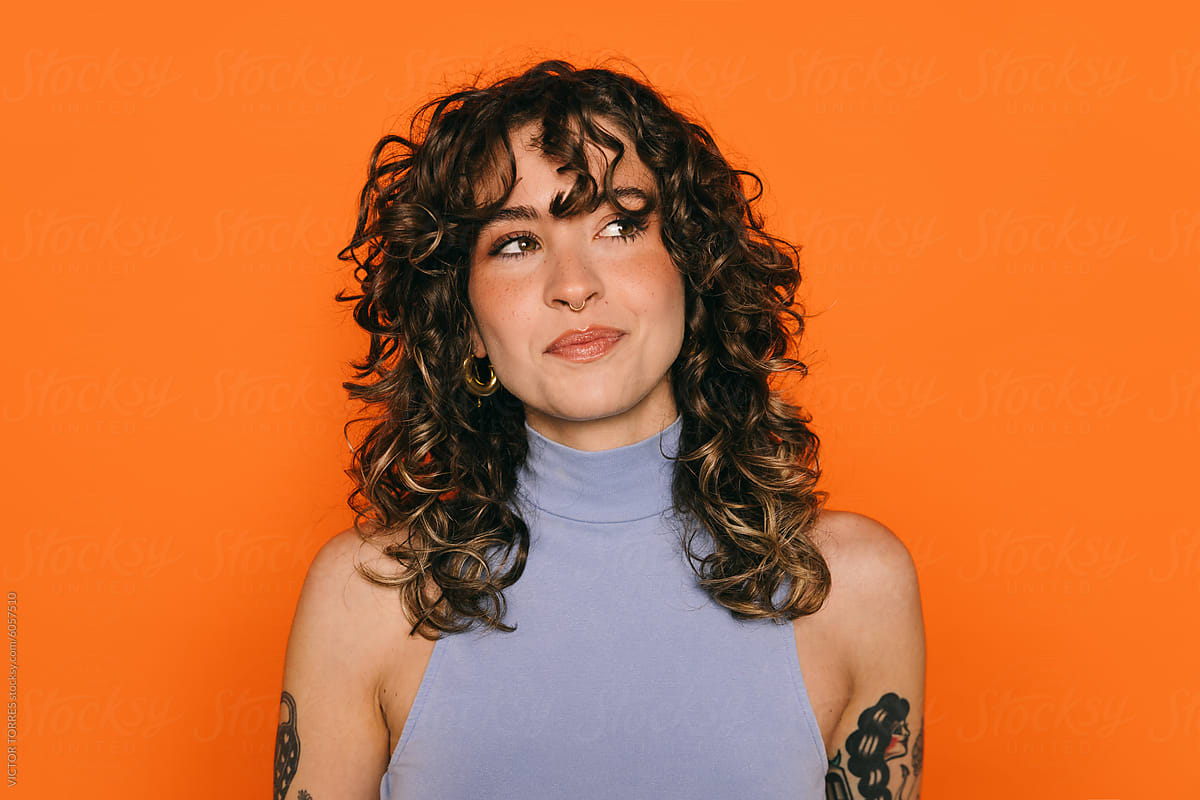 Stylish young woman with tattoos against orange background