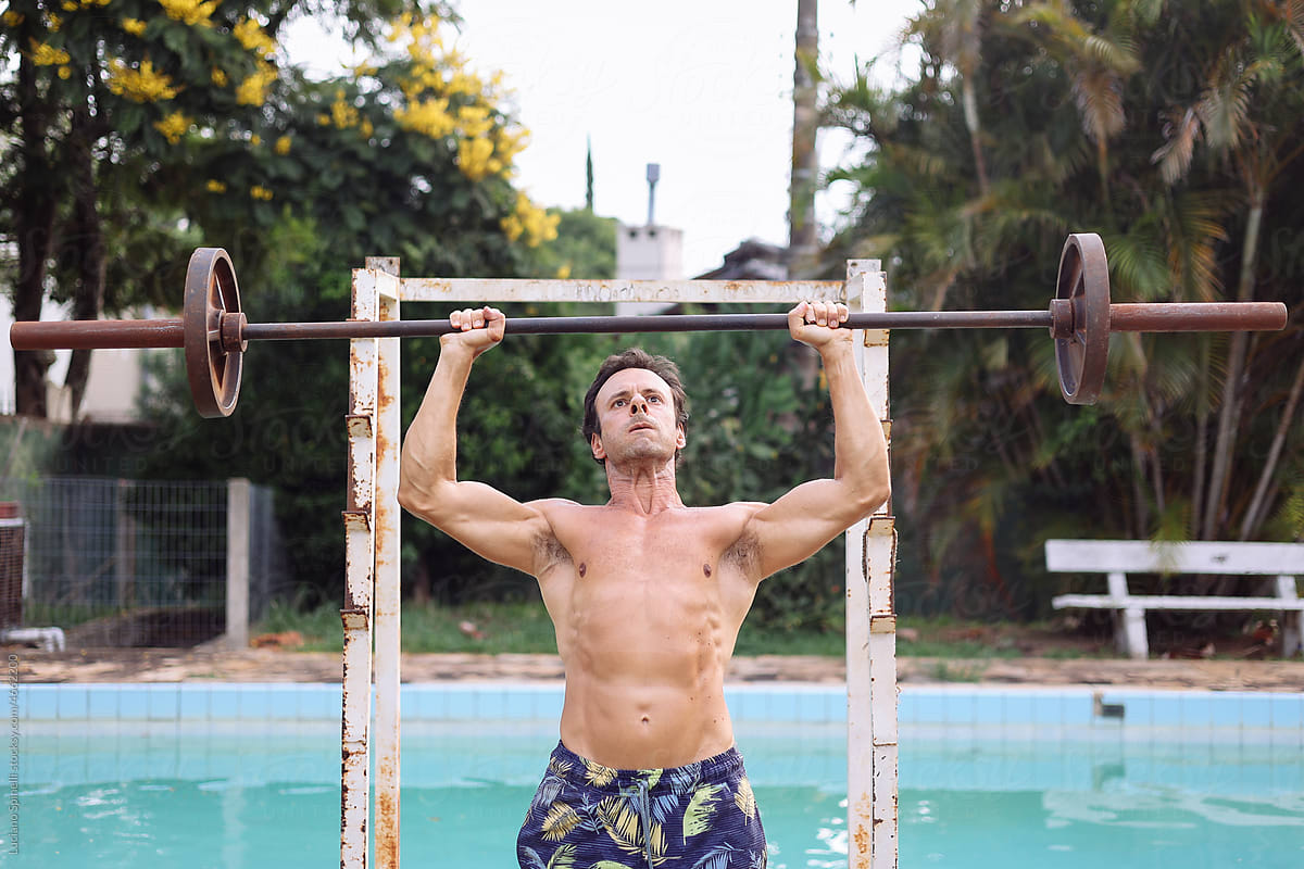 Bodybuilder doing weight lifting exercises in the garden by the pool