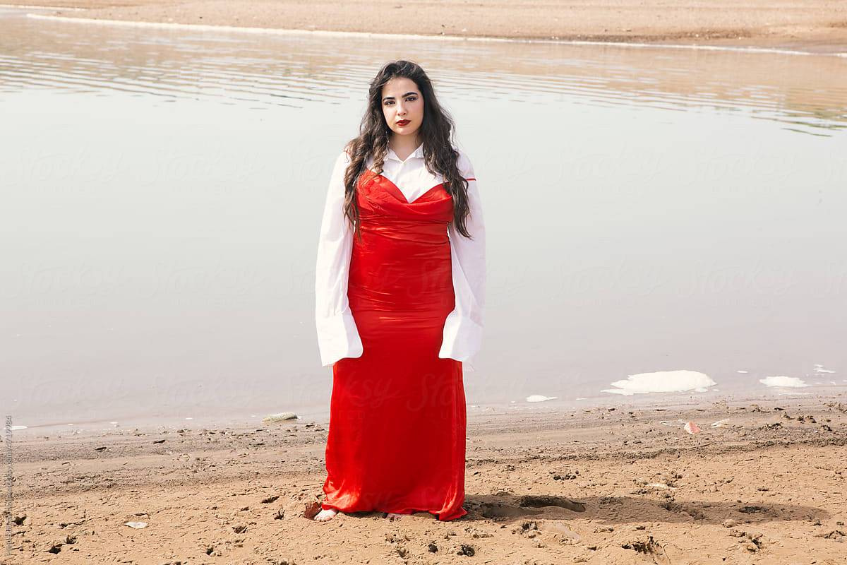 Young beautiful girl with long hair wearing red dress front of a river
