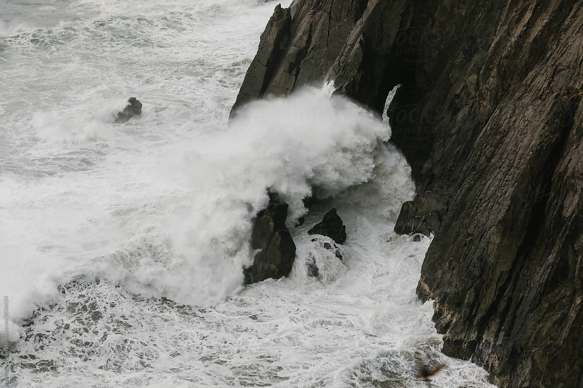 ocean wave crashing over dark rocky cliffs