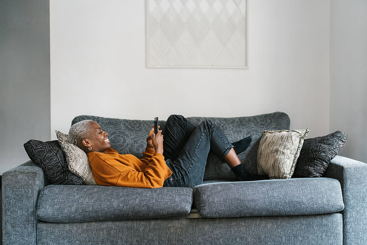 Glad woman lying on couch and using phone