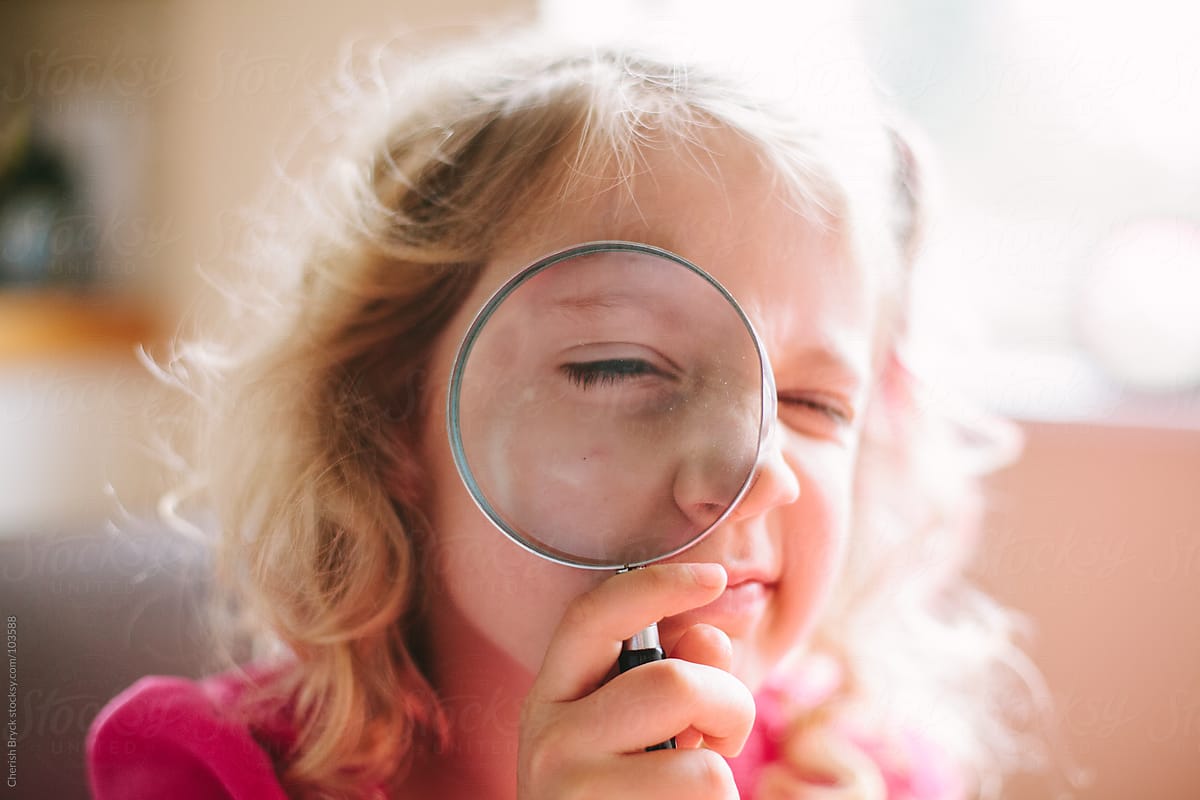 A girl holds a magnifying glass up to her face.
