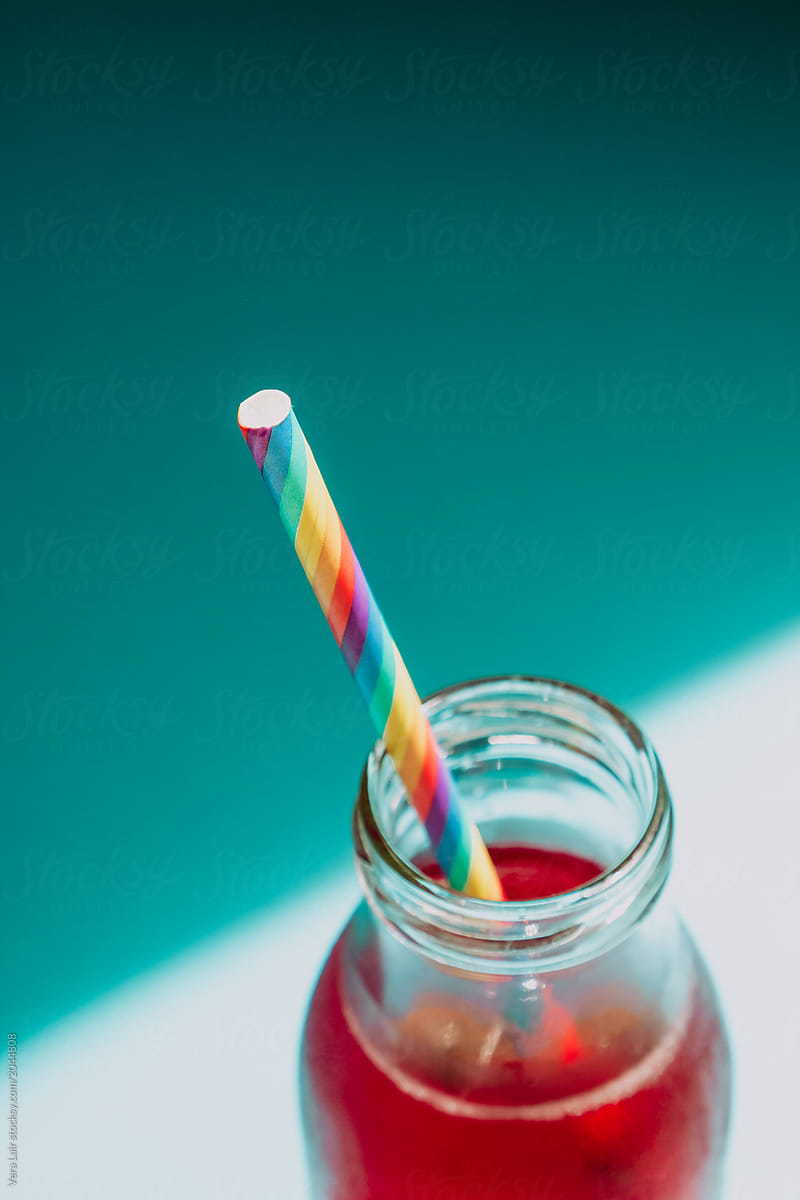 Striped straws with rainbow flag colours in a bottle with red soda on blue background
