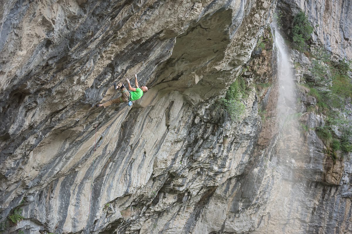 Caucasian male rock climber going up on steep rock wall