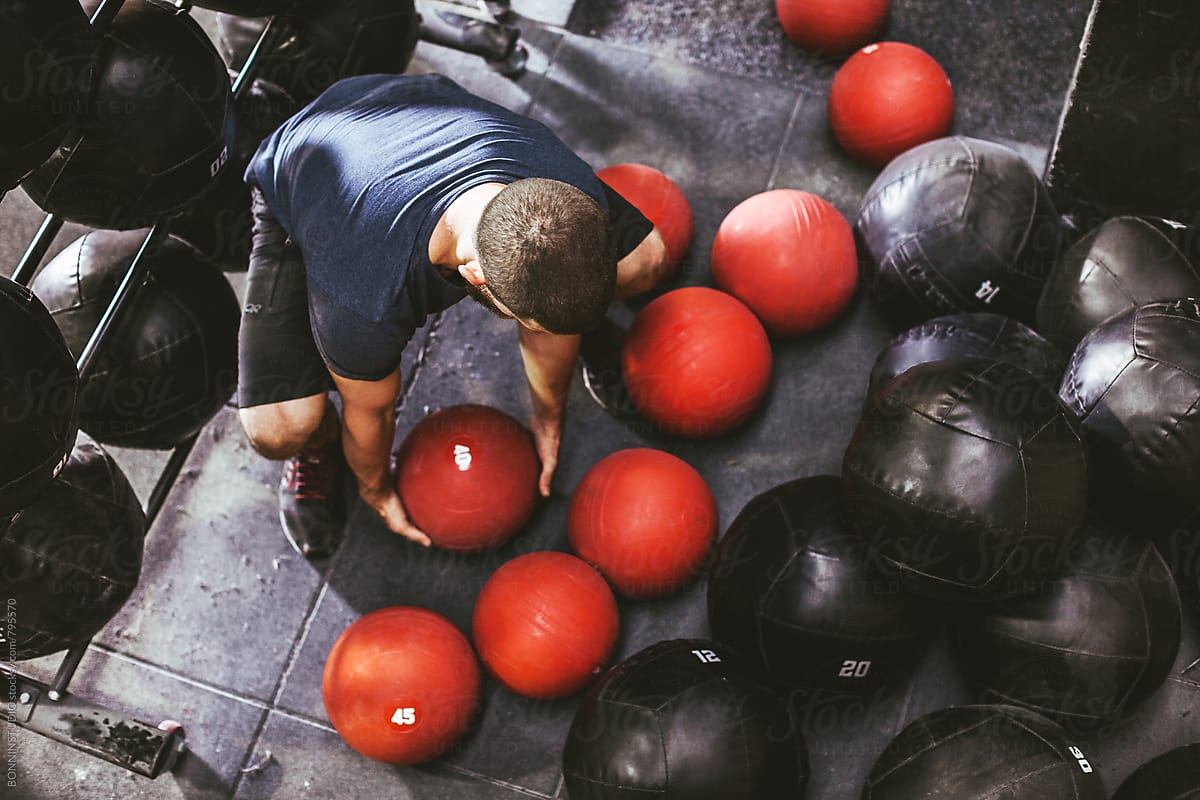 Overhead of a man lifting a red weighted ball in a gym.