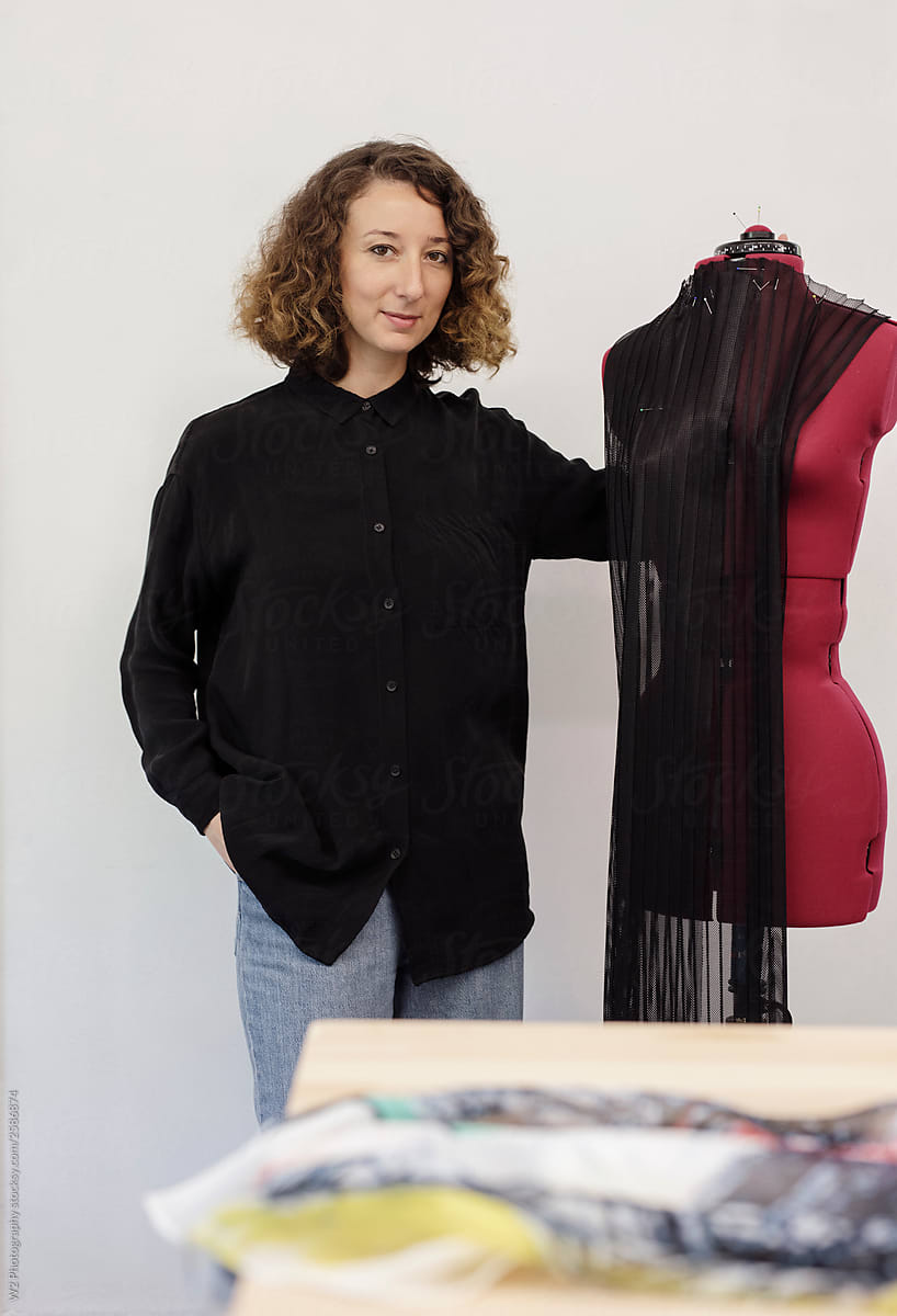 Portrait of a stylish fashion designer in her atelier with a dress form.