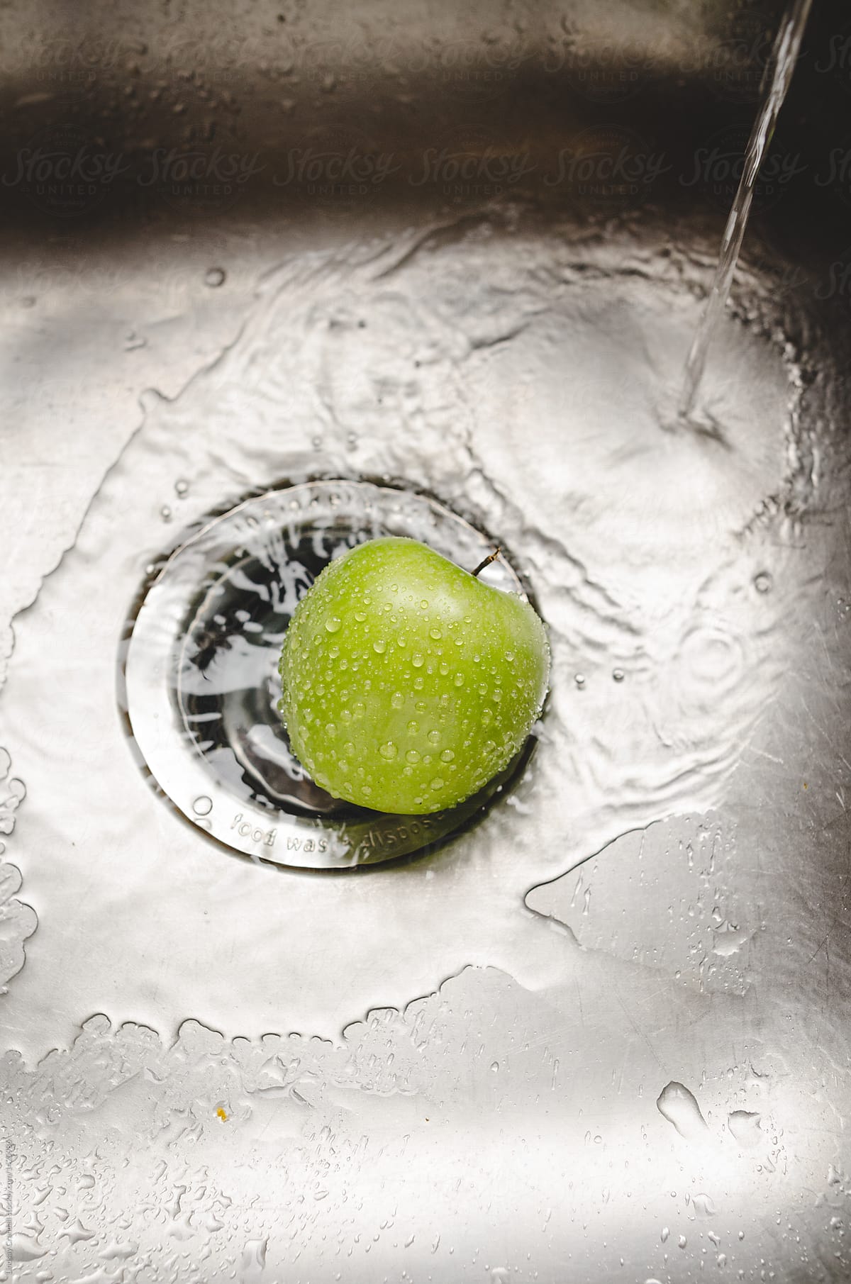 One green apple getting rinsed in the sink