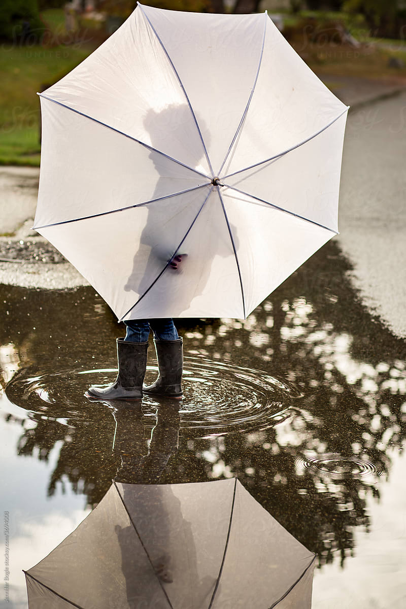 Boy with umbrella stands in puddle