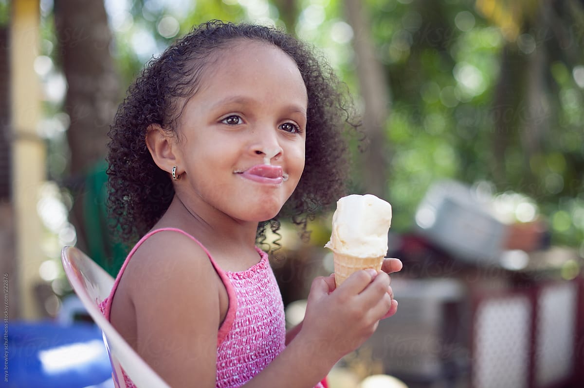 Child with curly brown hair licking ice cream