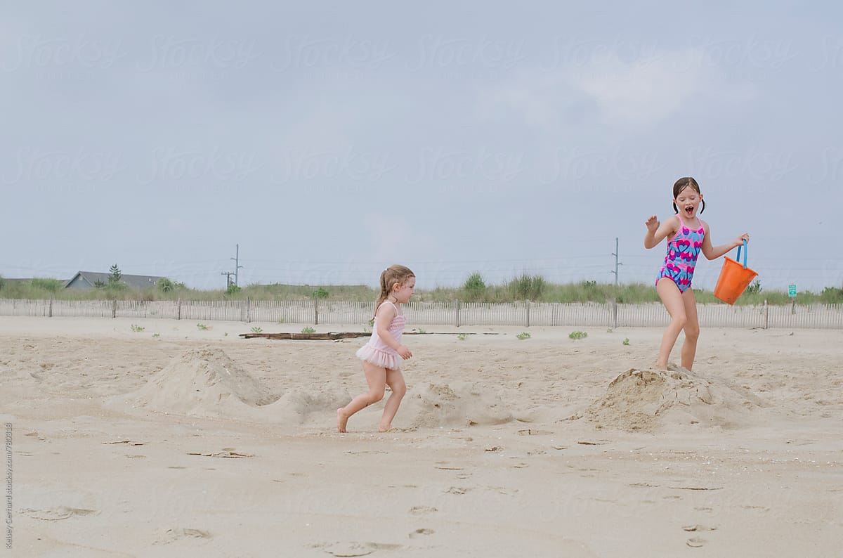 Two sisters run and play on a sandy beach dune.