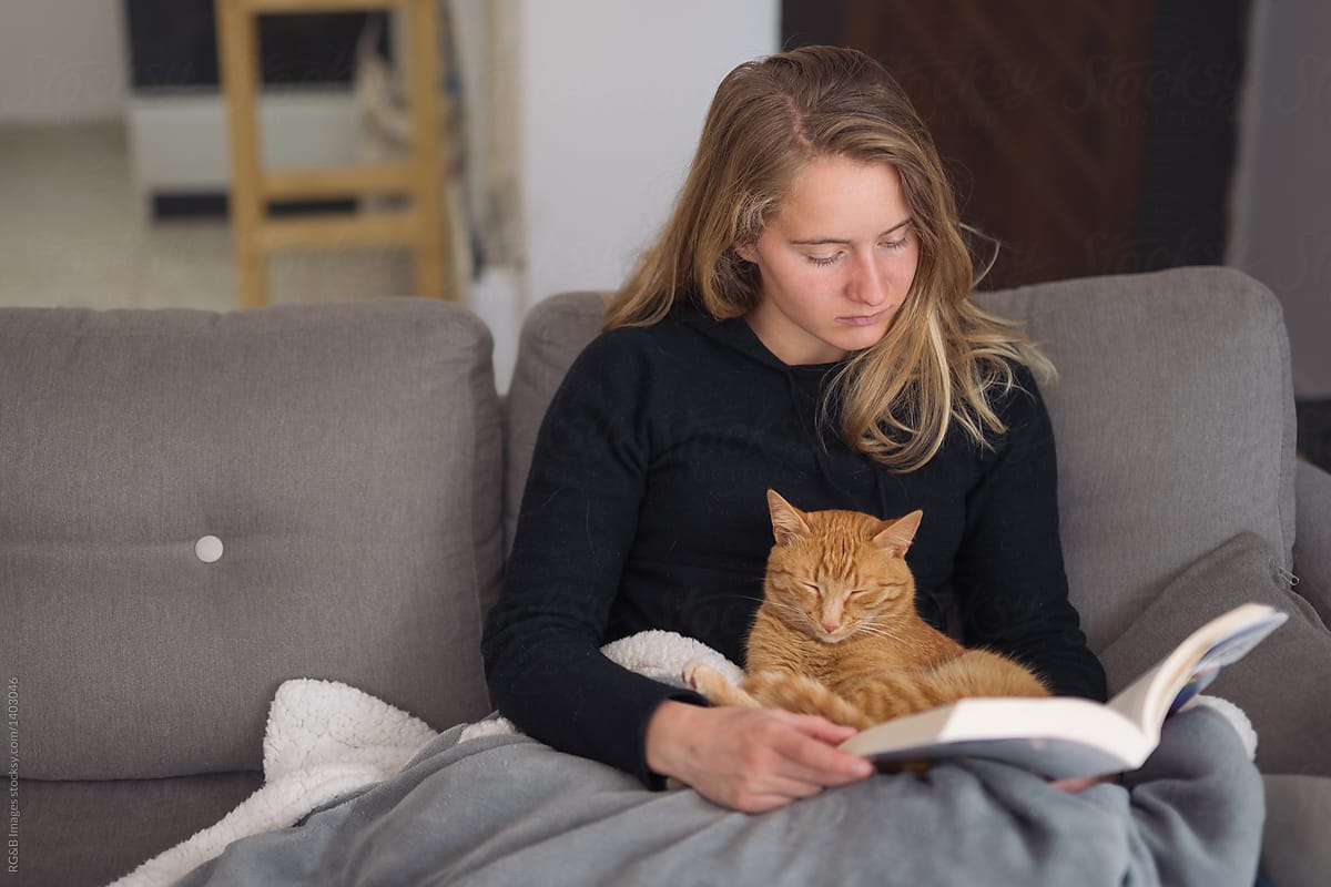 Woman reading a book with her cat sitting on  sofa