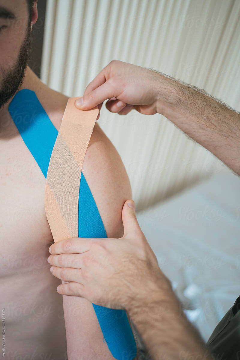 Doctor sticking kinesio tapes on shoulder