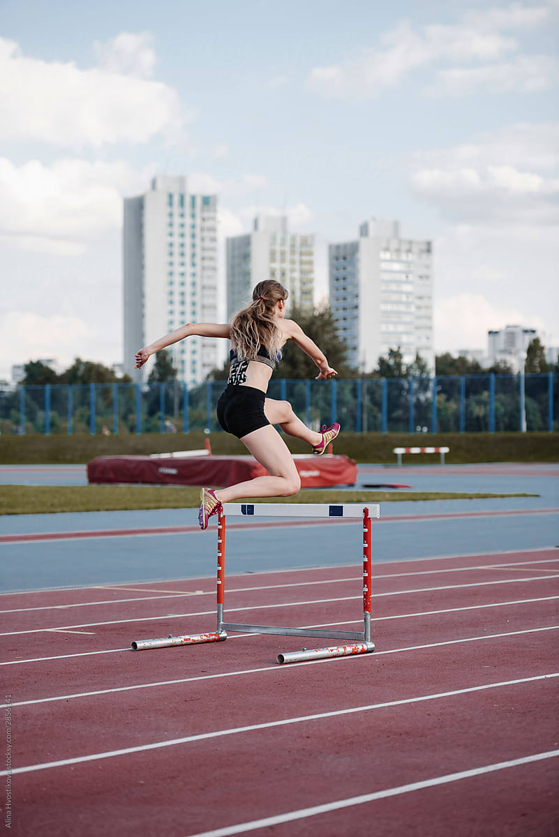 Successful sportswoman jumping over hurdle at stadium