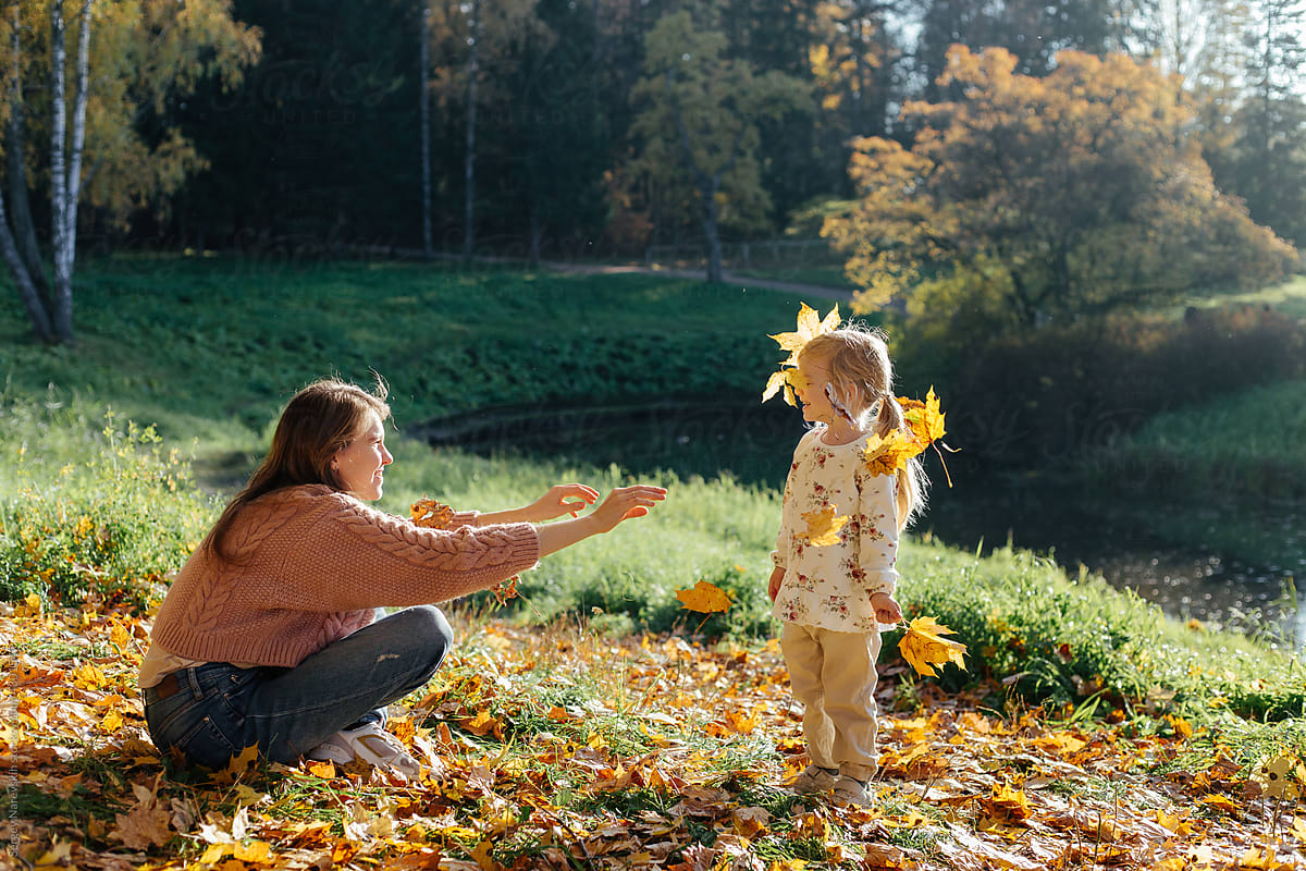 Mother throwing yellow leaves to daughter in park