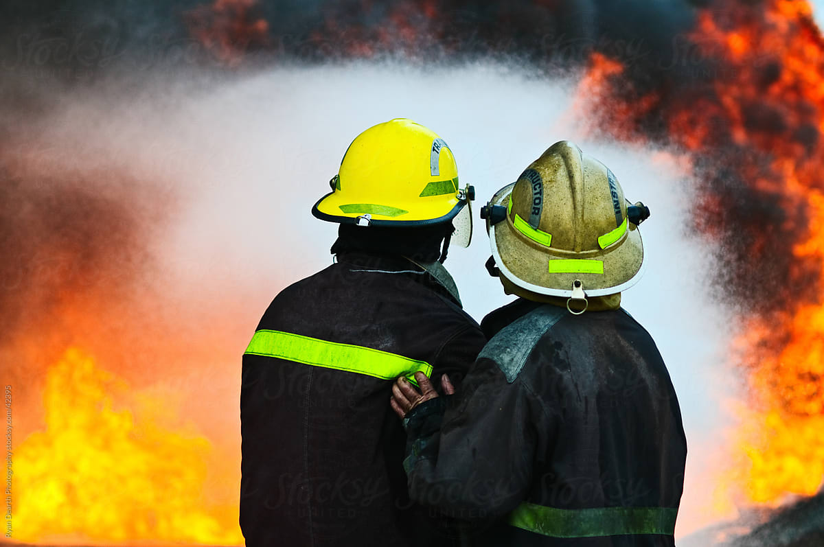 A firefighting instructor and trainee against a wall of flames