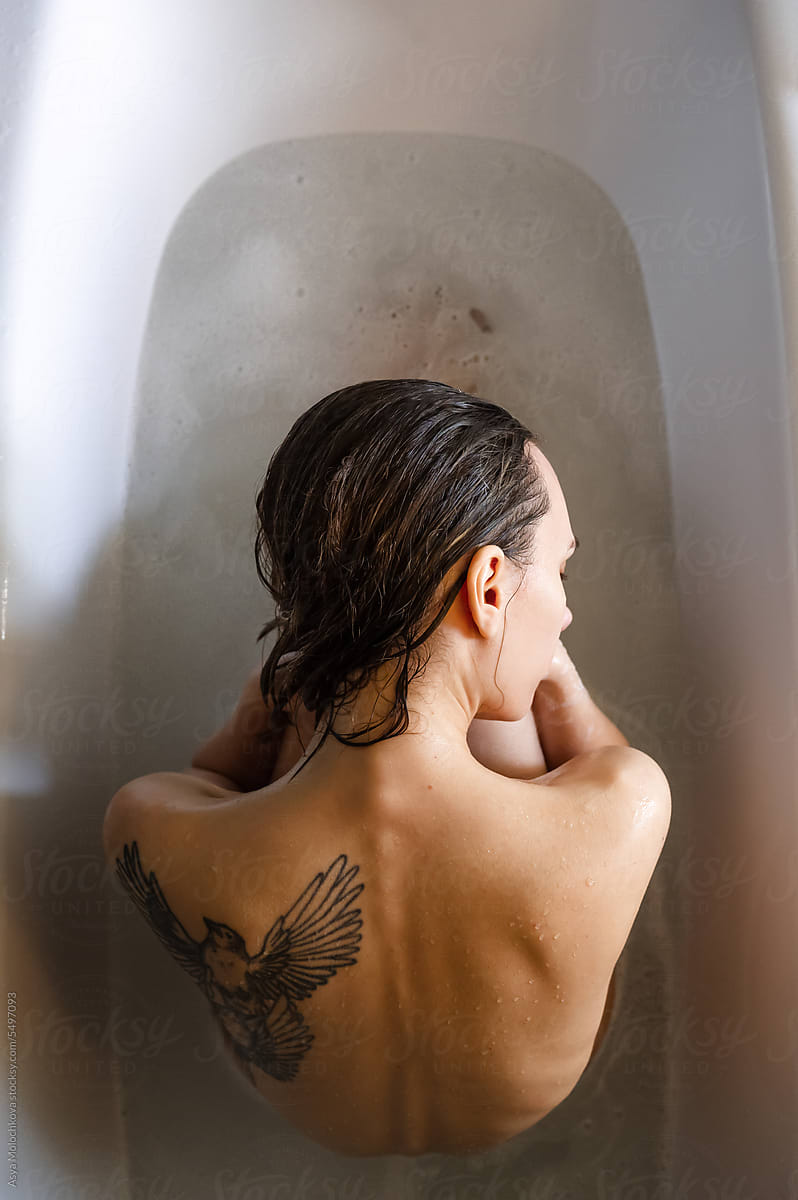 Portrait of a woman with tattoo on a back sitting in a bathroom