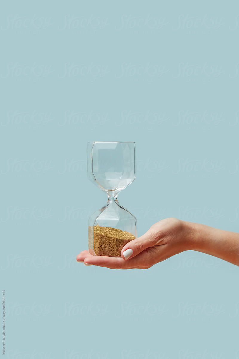 Sandglass with golden sand held by woman's hand.
