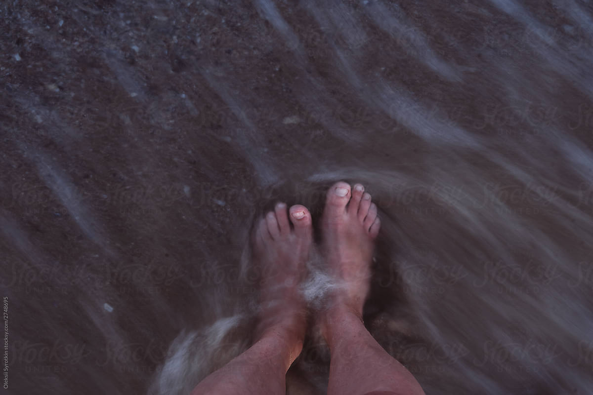 Anonymous person standing barefoot under sea water.