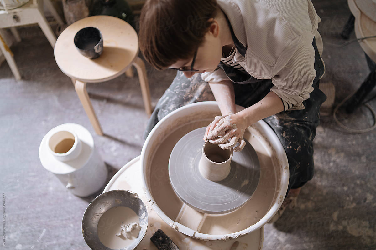 Young woman creating clay vase on wheel