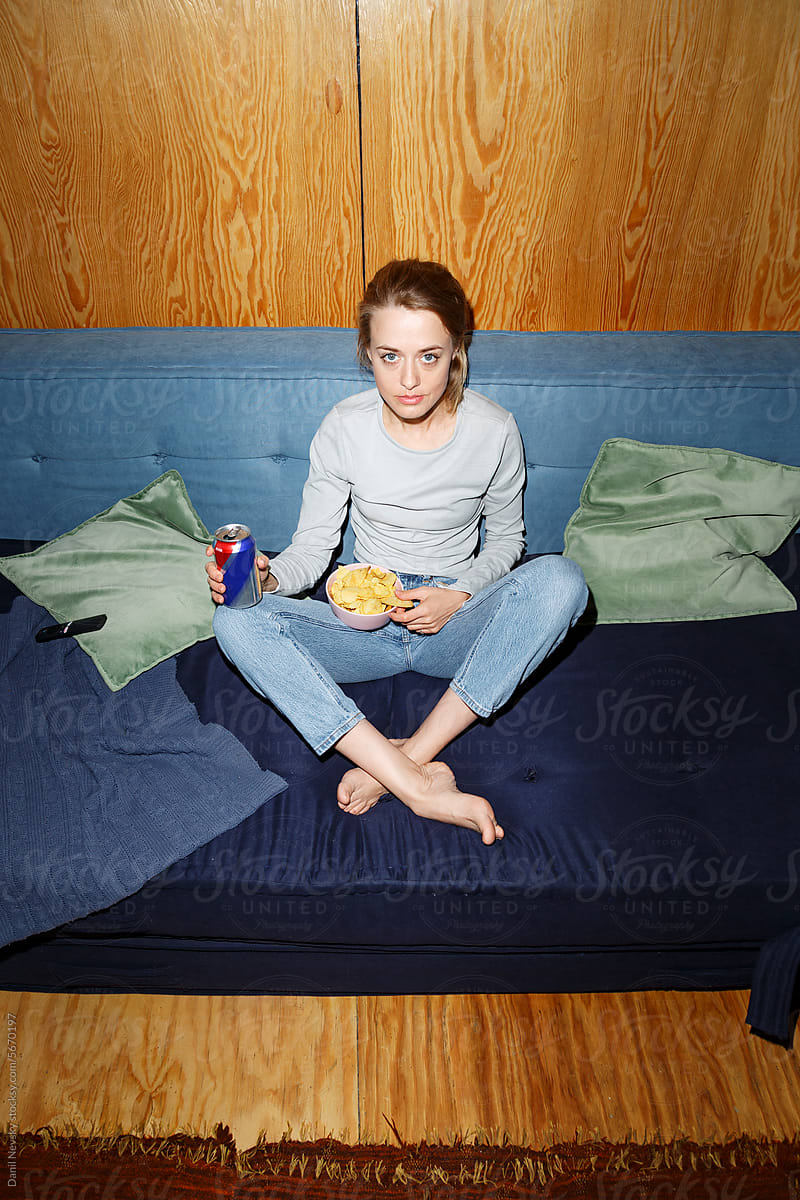 Woman sitting on sofa eating chips and drinking soda