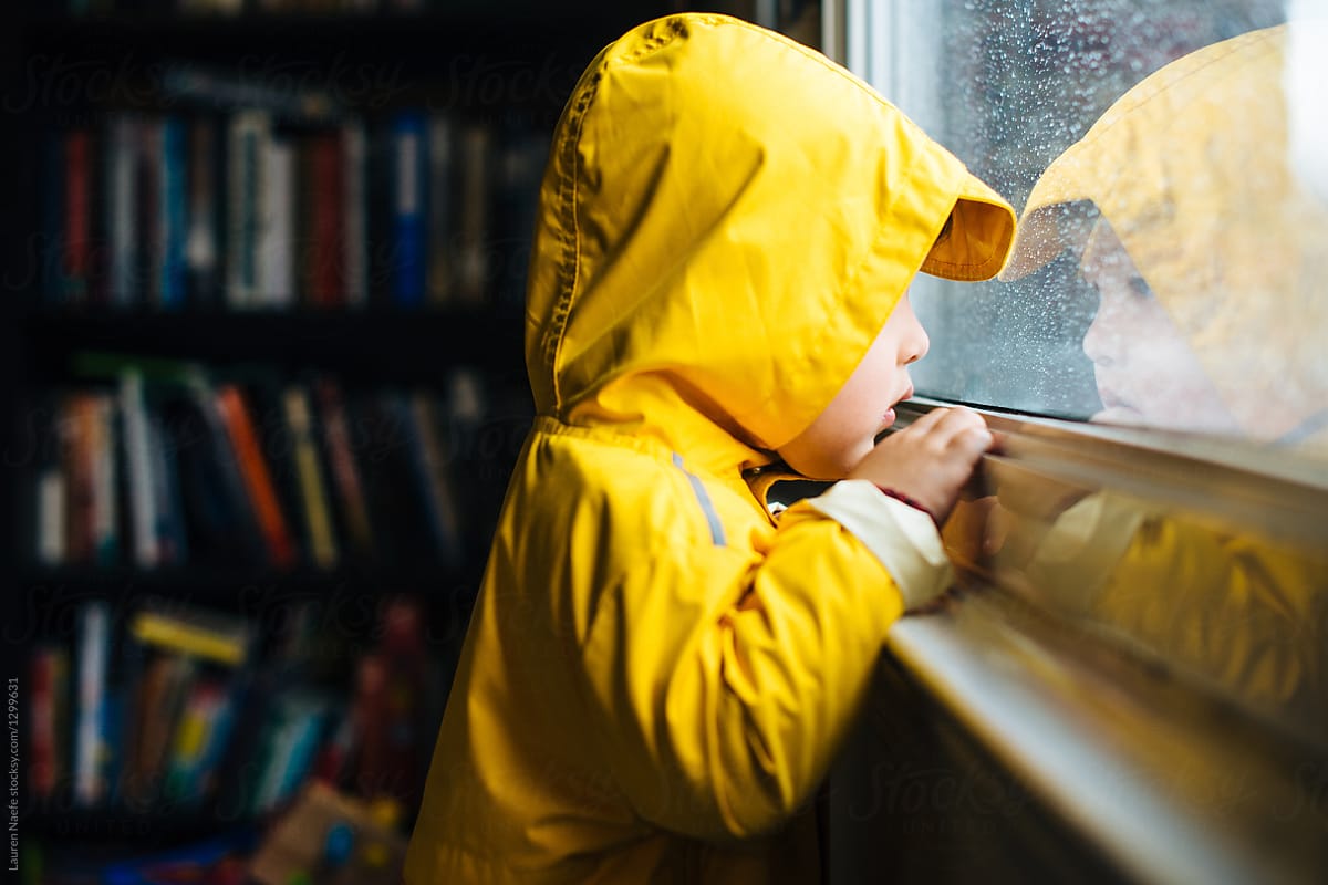Little kid in raincoat watching rain