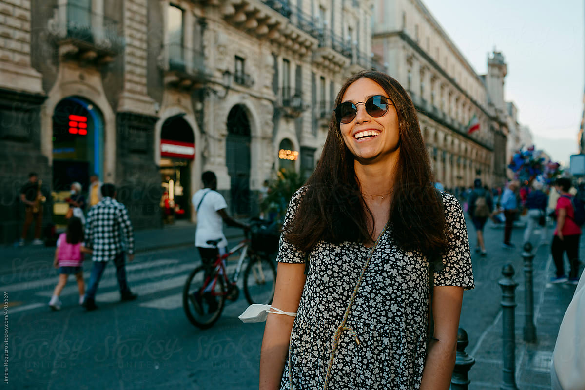 Attractive woman with sunglasses in sunlight in city street smiling.