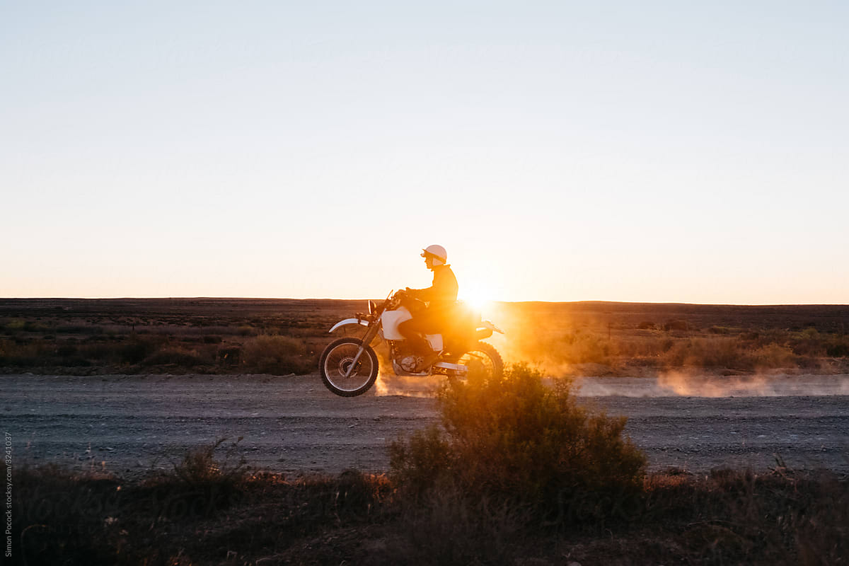 Motorcycle rides along a dusty desert road at sunset